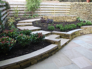 yorkshire garden with dry stone wall, low stone retaining wall and curved low stone steps and timber fence